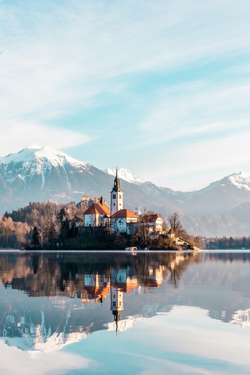 brown and white concrete building near body of water and mountain under white clouds and blue