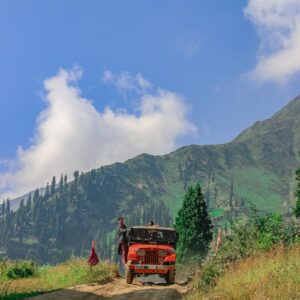 red truck on green grass field near mountain under blue sky during daytime